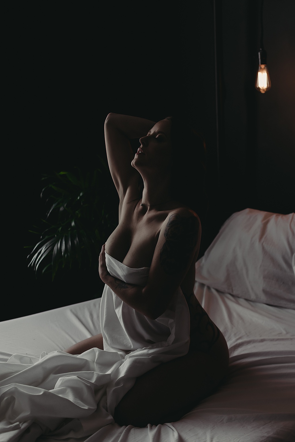 woman sitting in bed wrapped in a white sheet for Grand Haven MI boudoir shoot