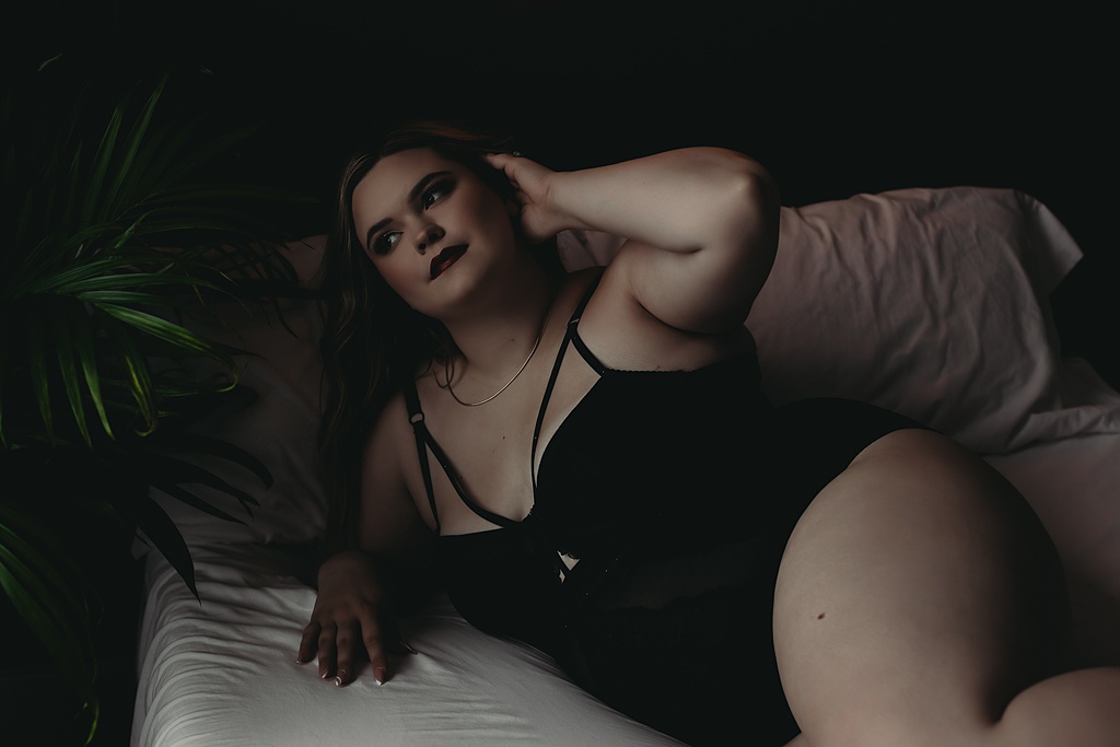 woman laying in bed wearing black bodysuit for Grand Haven Michigan boudoir shoot