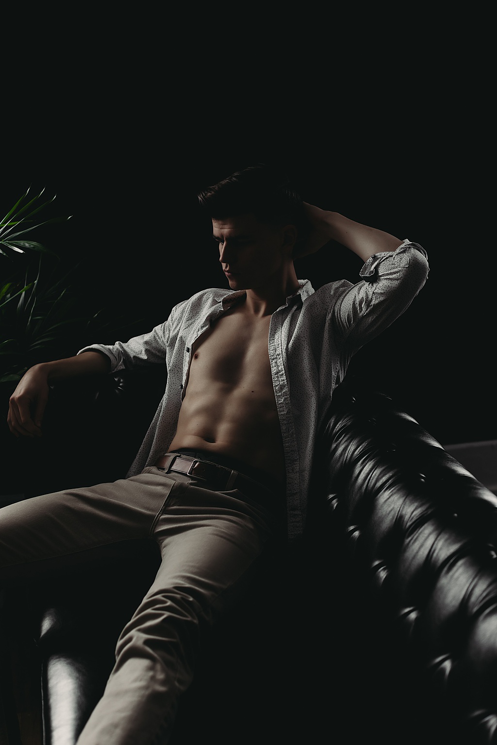 men's boudoir picture of a man sitting on a black leather couch